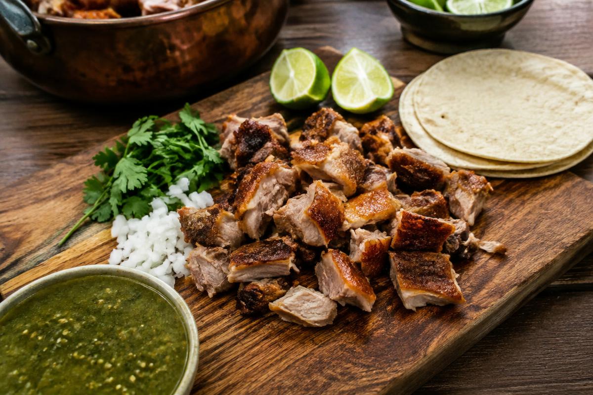 Crispy chopped Michoacán carnitas on a board with tortillas, lime and salsa verde